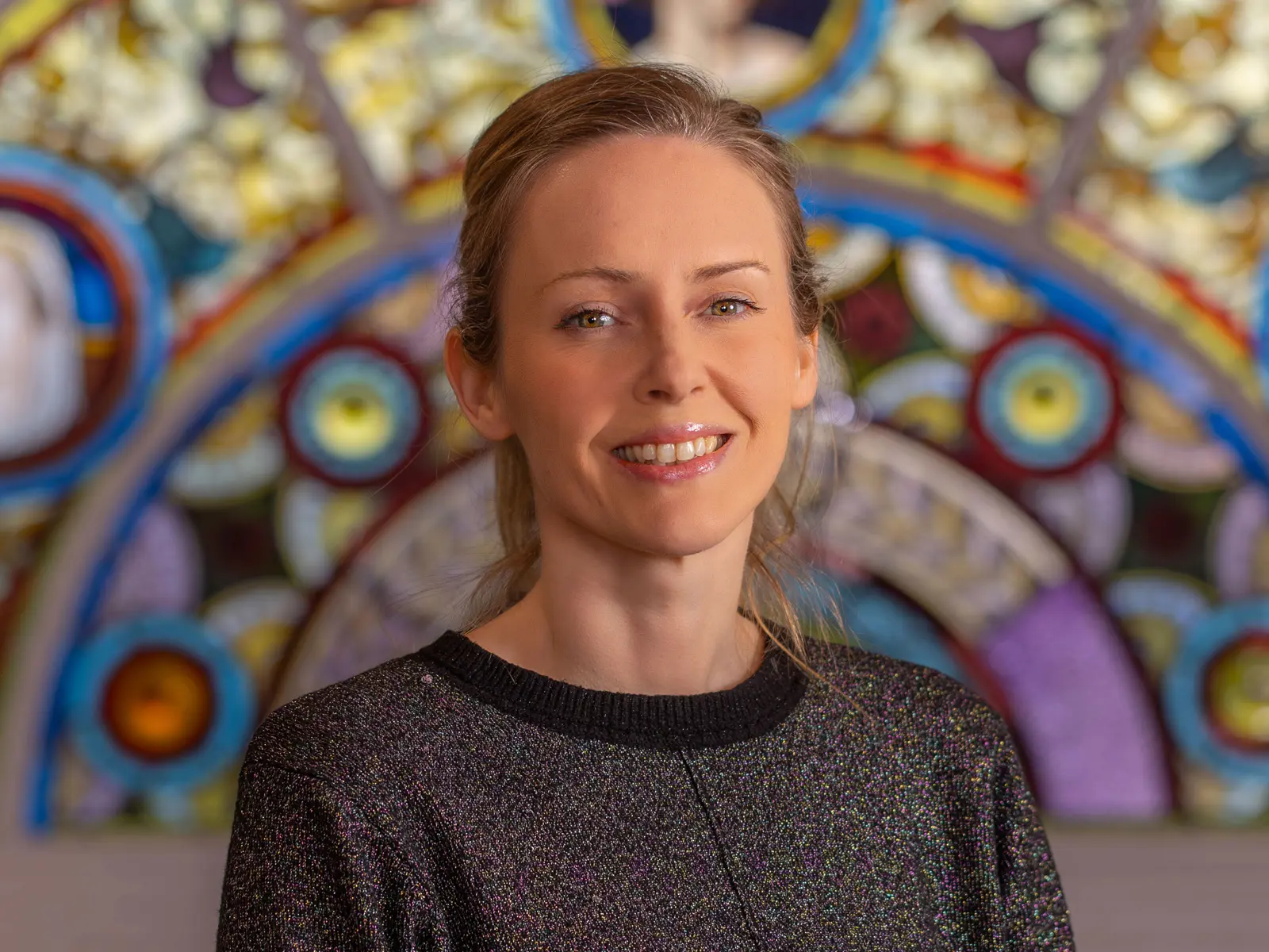 Blond woman smiling in front of stain glass window