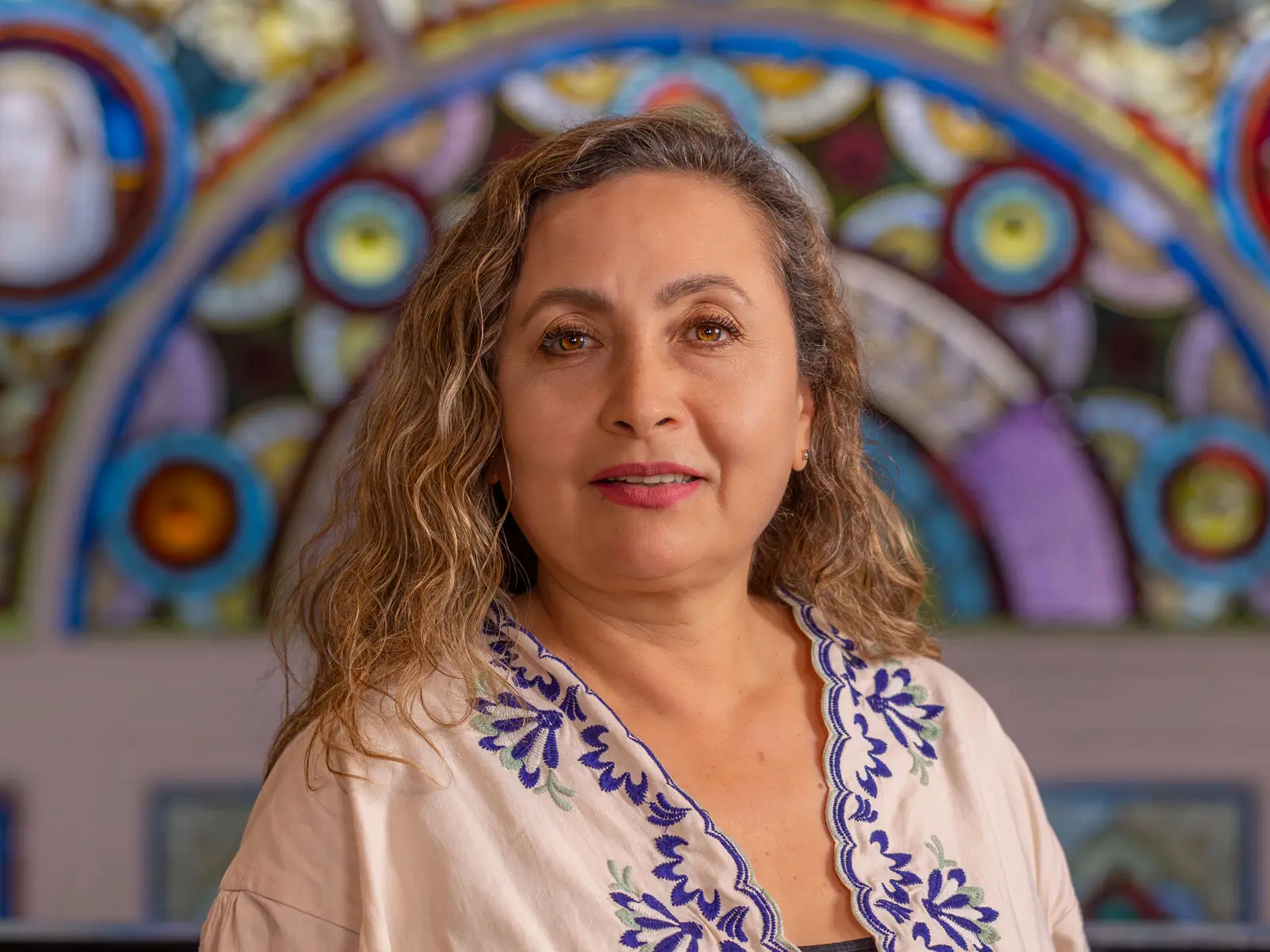 Curly haired woman in white and blue blouse in front of stain glass window