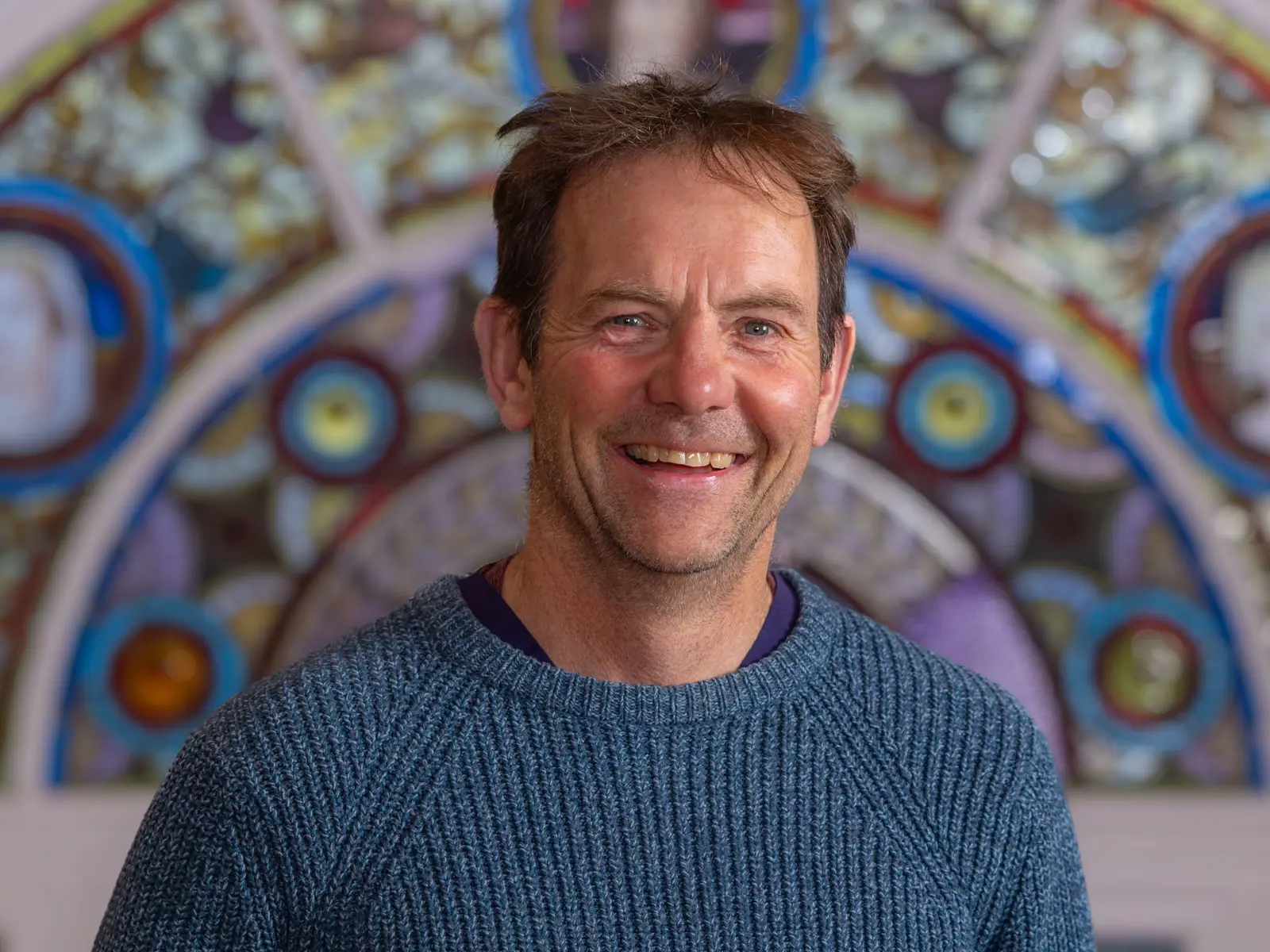 Smiling man in blue jumper in front of stain glass window