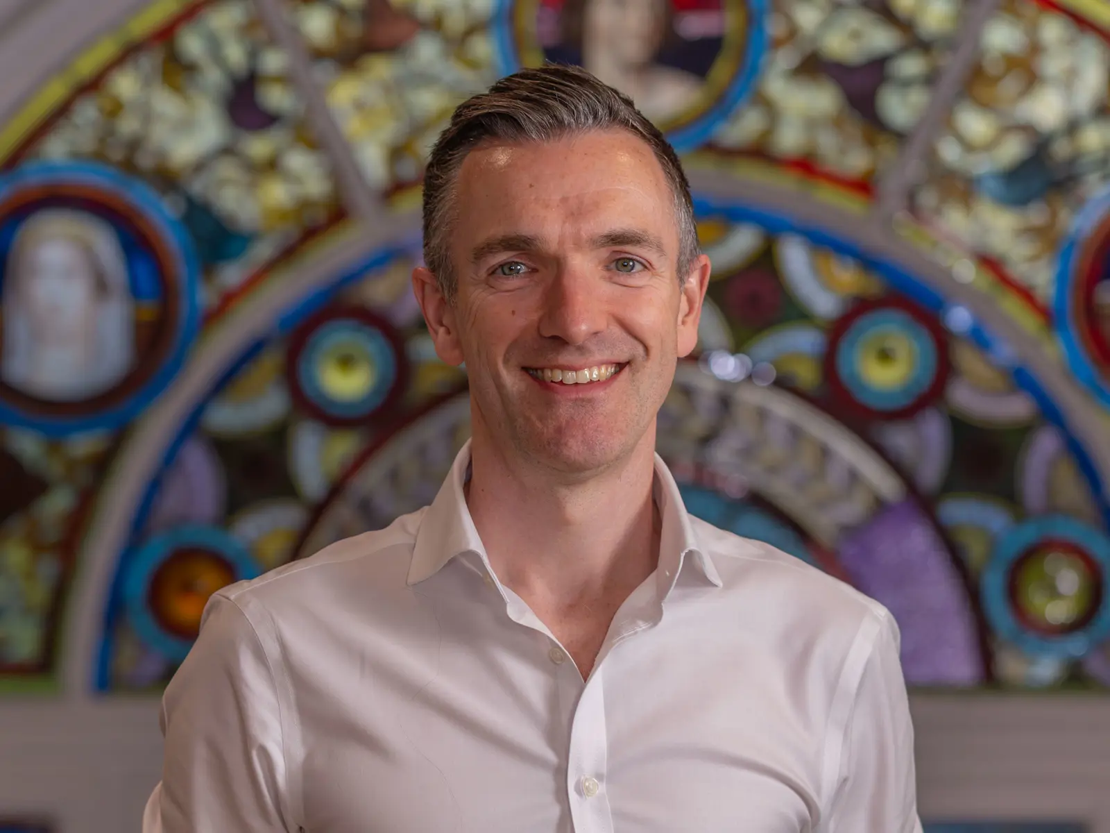 Short grey haired in white shirt in front of stain glass window