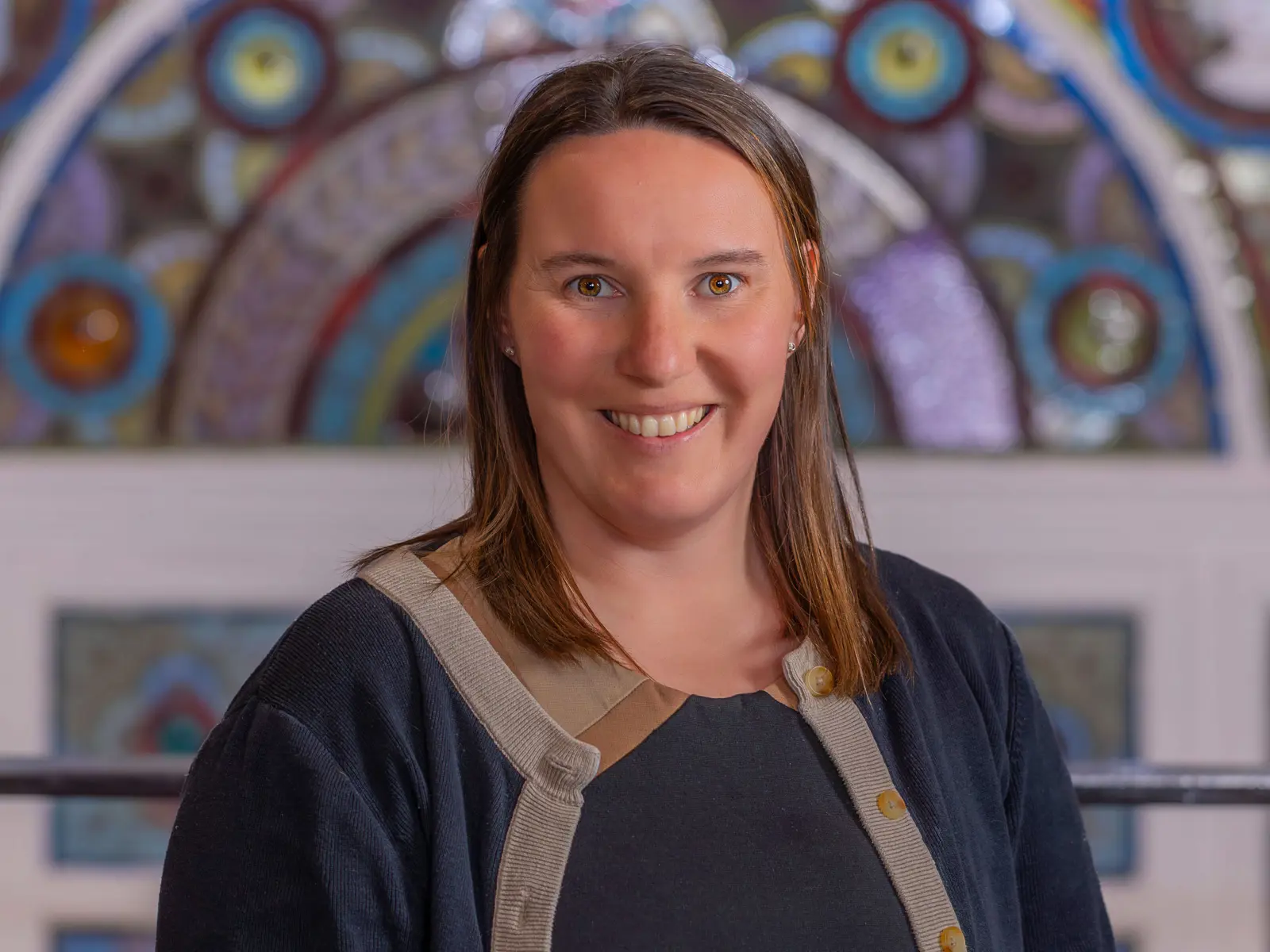 Smiling lady with medium length brown hair in front of stain glass window