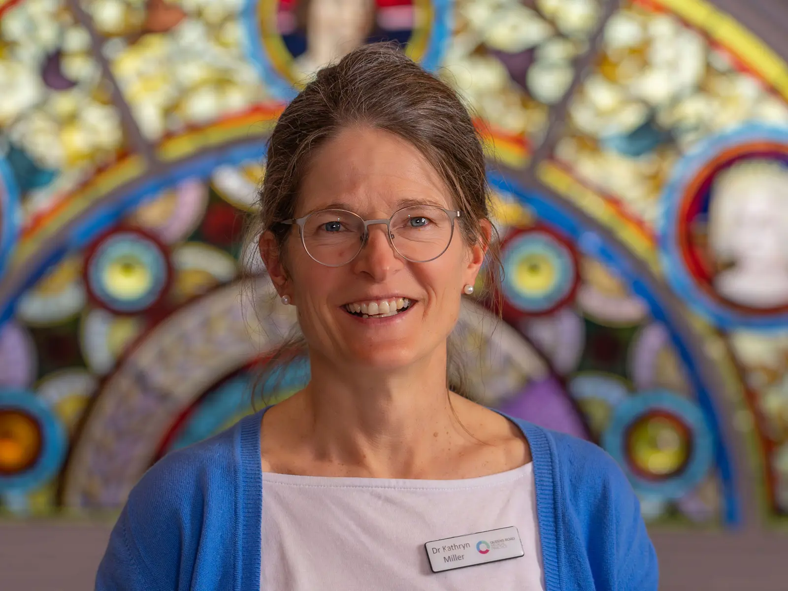 Smiling woman in front of stain glass window wearing white blouse with blue cardigan
