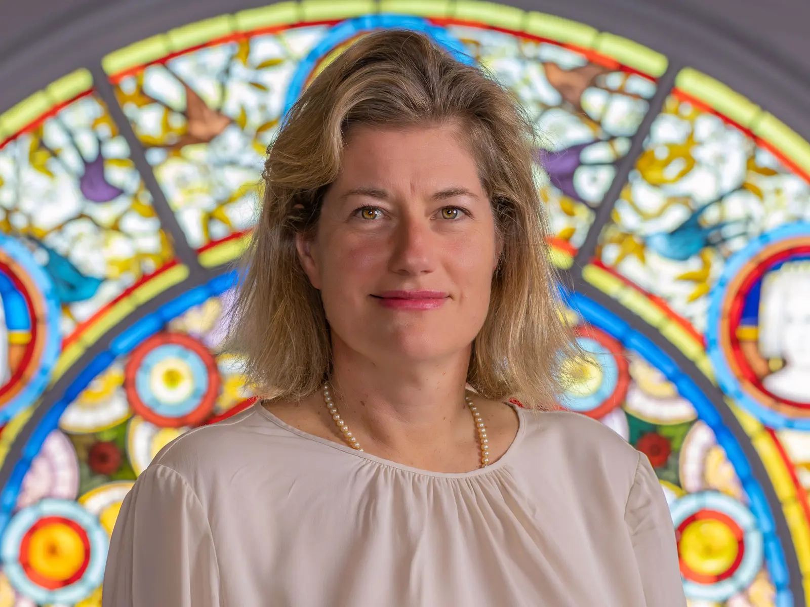 Blond short haired woman standing in front of stain glass window
