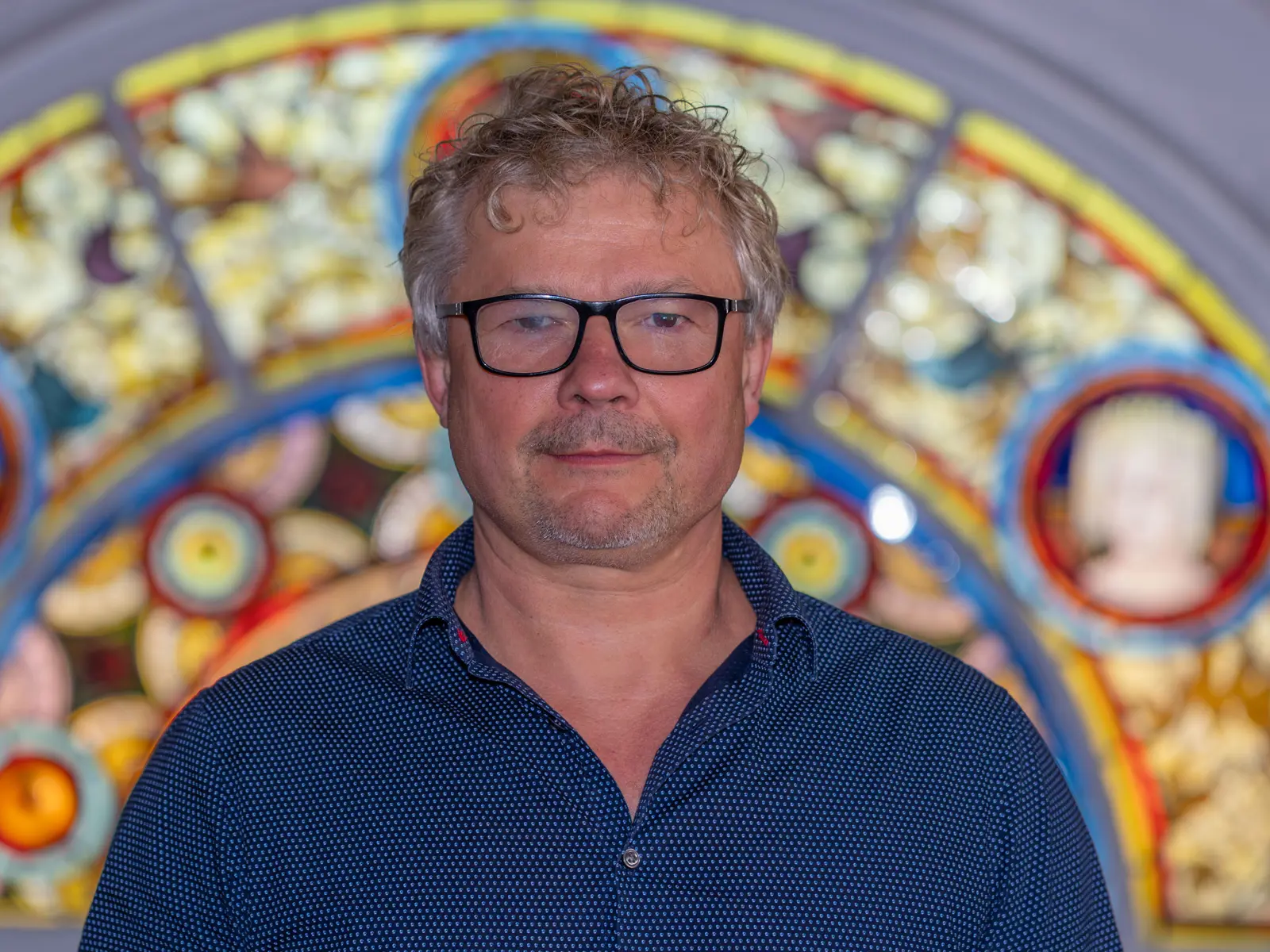 Smiling grey haired man in front of stain glass window