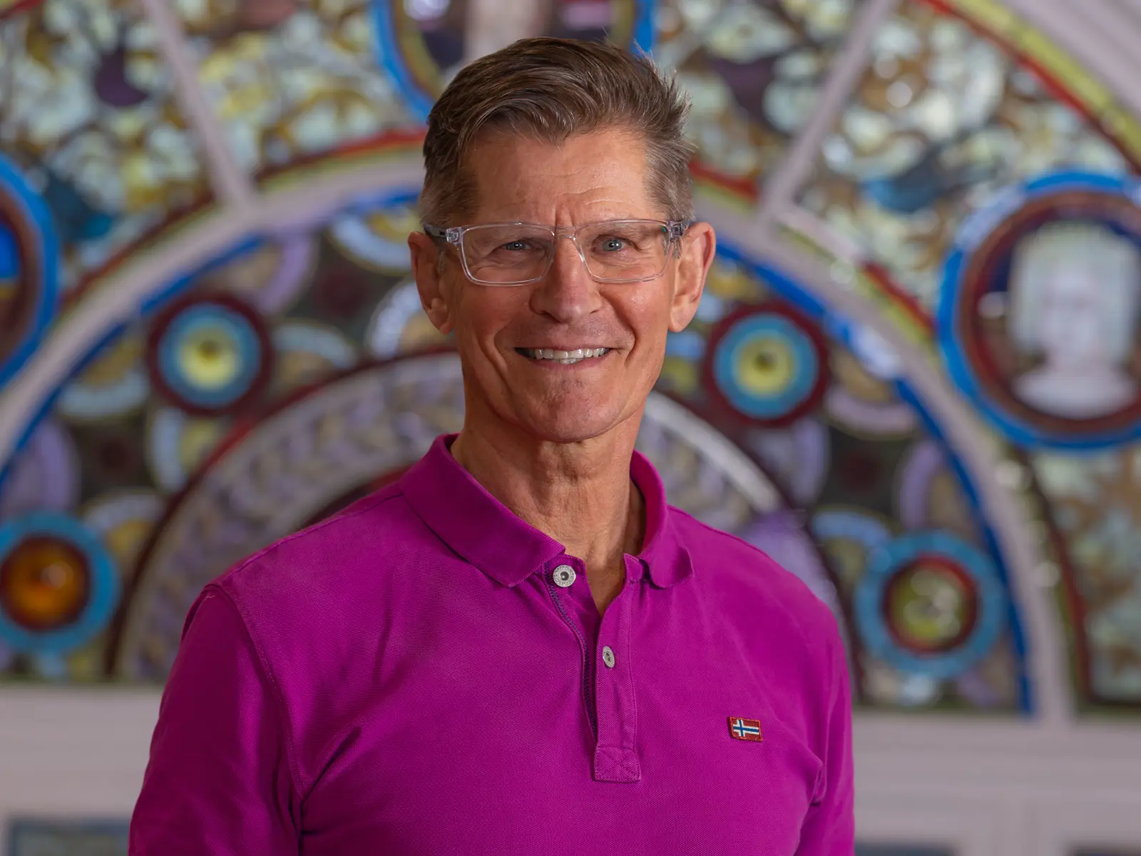 Smiling man in glasses and pink shirt in front of stain glass window
